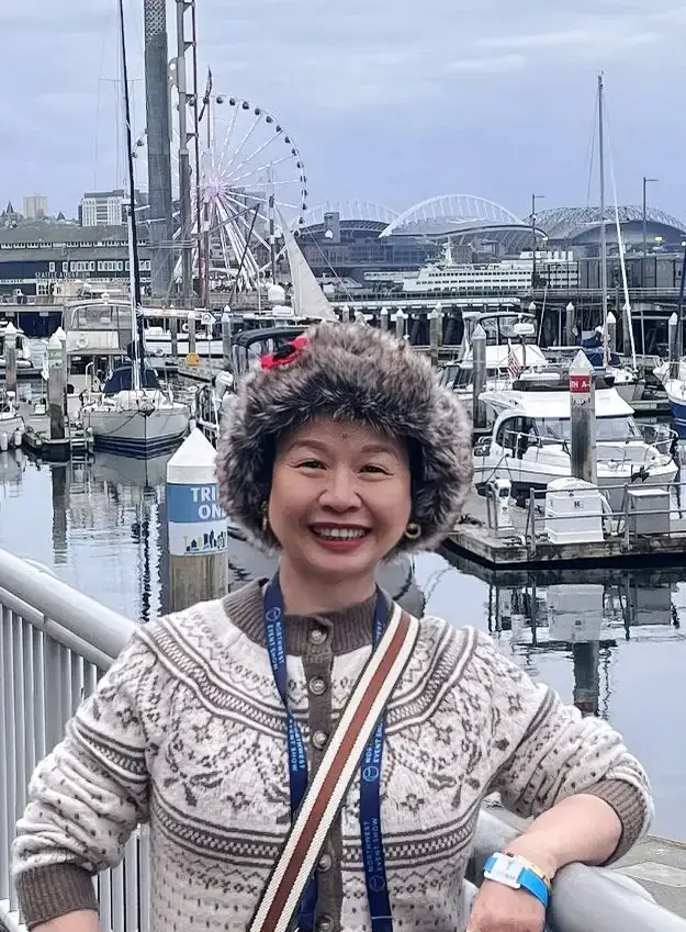 Jackie Wu in a Fair Isle sweater and fur hat on a Seattle waterfront pier at the Northwest Event Show, boats and the city behind her